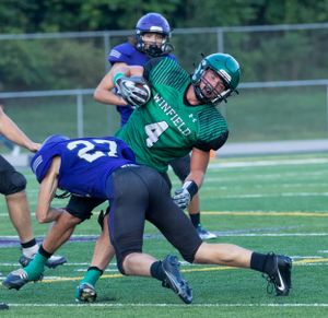Defensive tackle in green uniform takes down opposing player in blue uniform.
