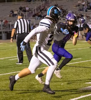Football players from opposing teams compete during nighttime game on artificial turf.