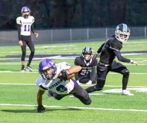 Football player dives to make a tackle during nighttime game on artificial turf.