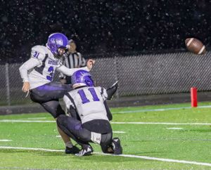 Football players collide during rainy night game on artificial turf.
