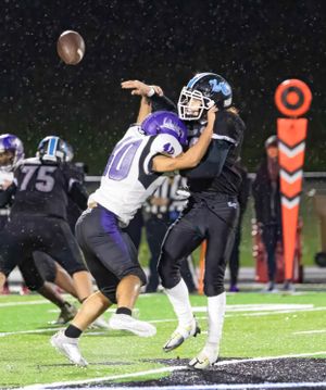 Players compete for airborne football during nighttime game with yard markers visible.