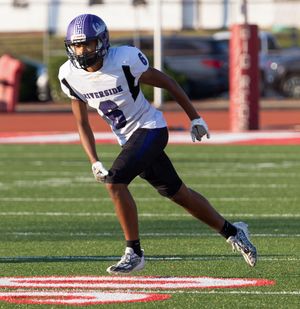 Football player in purple and white uniform demonstrates athletic stance on field.