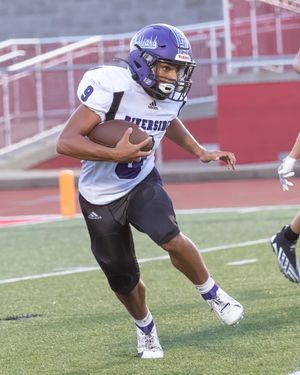 Football player carries ball during gameplay wearing purple and white uniform.