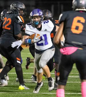 Running back carries football through defensive line during nighttime football game.