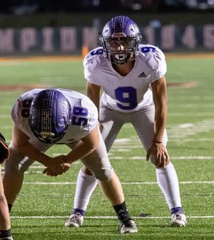 Two football players in white uniforms with purple helmets prepare for snap during game.