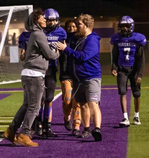 Coaches and players interact on sideline during football game.