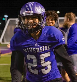 Football player in purple Riverside jersey stands on field during night game.