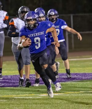 Football player in blue uniform runs with ball during nighttime game on purple field.