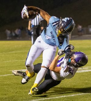 Football player in light blue uniform tackles opponent in purple jersey during night game.