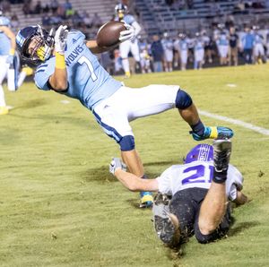 Player in light blue uniform dives over defender during football game.
