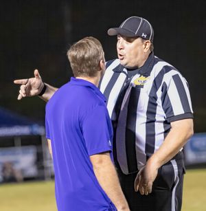 A football referee in striped uniform discusses with coach during nighttime game.