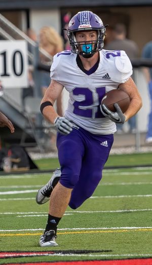 Running back in white and purple uniform carries football during game action.
