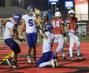 Football players from purple and red teams interact on the field during a night game.