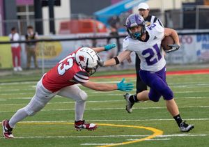 Football player in purple uniform evades tackle from defender in red jersey.