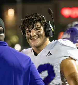 Player wearing headphones and white jersey smiles during a night football game.
