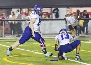 Two football players in purple uniforms execute a play on the field.