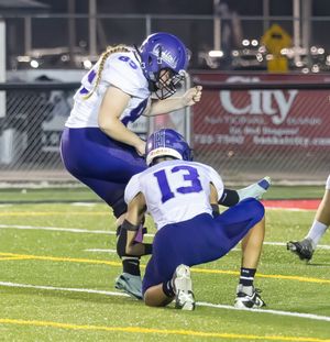 Football players in purple uniforms perform field goal attempt during game.