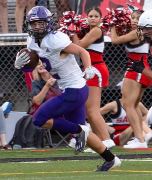 Football player in purple uniform runs with the ball past cheerleaders during a game.