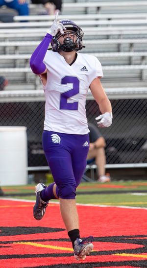 Football player in white uniform with purple number 2 celebrates on red endzone.