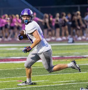 Player in white uniform runs with football during night game with cheerleaders in background.