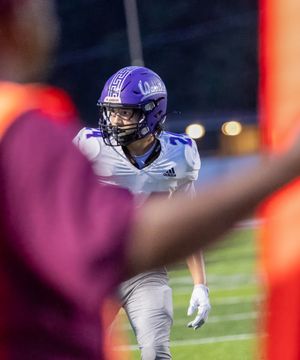 Football player in purple helmet and white jersey stands ready on field during night game.