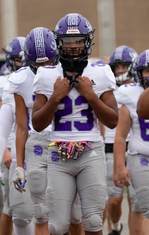 Football player in white uniform adjusts equipment before game.