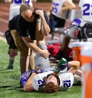 Athletic trainer provides medical attention to injured football player on sideline during game.