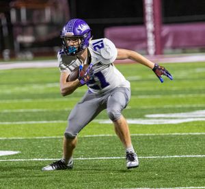 Football player in purple and white uniform carries ball while making offensive move.