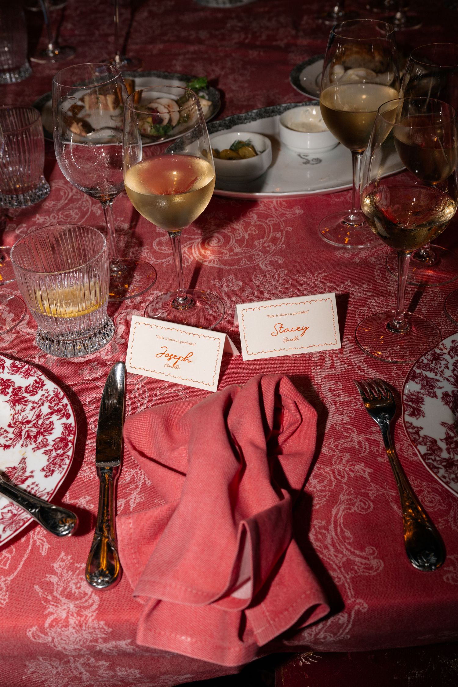 Place settings with pink napkins and name cards on a red damask tablecloth at an elegant dinner party.