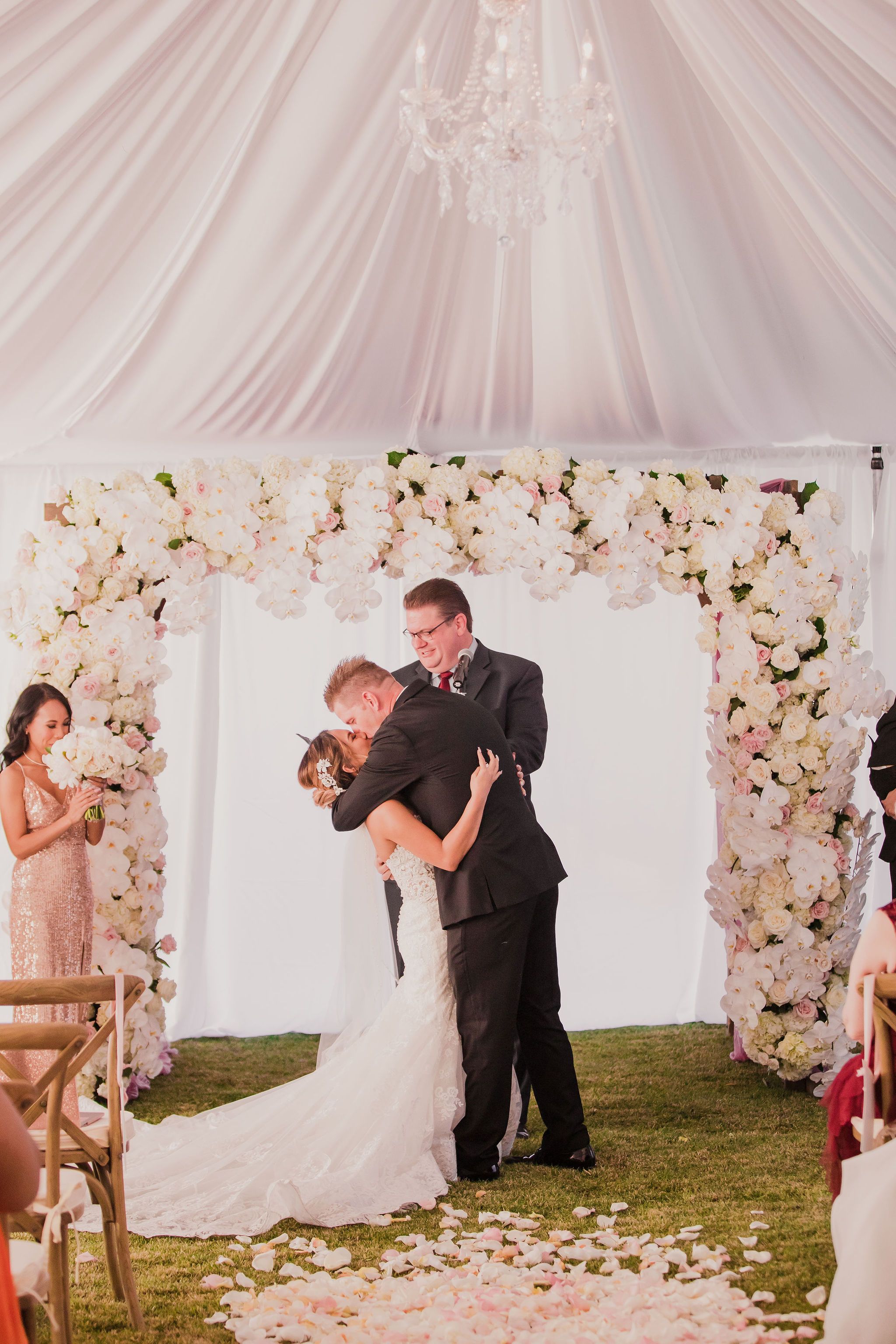 A romantic wedding ceremony sequence showing a couple's first kiss under a draped white tent with floral decorations.