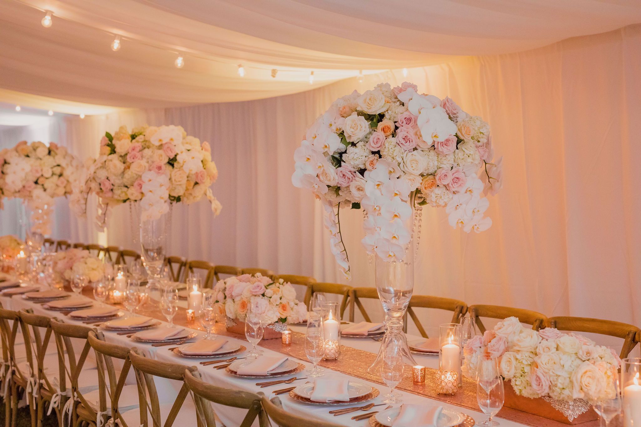 Elegant wedding reception setup with blush pink lighting and white floral centerpieces on long dining tables.