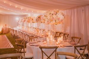 Elegant wedding reception table setting with pink floral centerpieces and string lights under white tent draping.