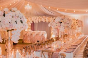 Elegant wedding reception hall with long tables decorated in white orchids and crystal chandeliers under warm lighting.