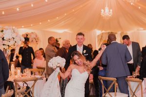 Wedding guests enjoy an elegant reception under a white tent with crystal chandeliers and string lights.