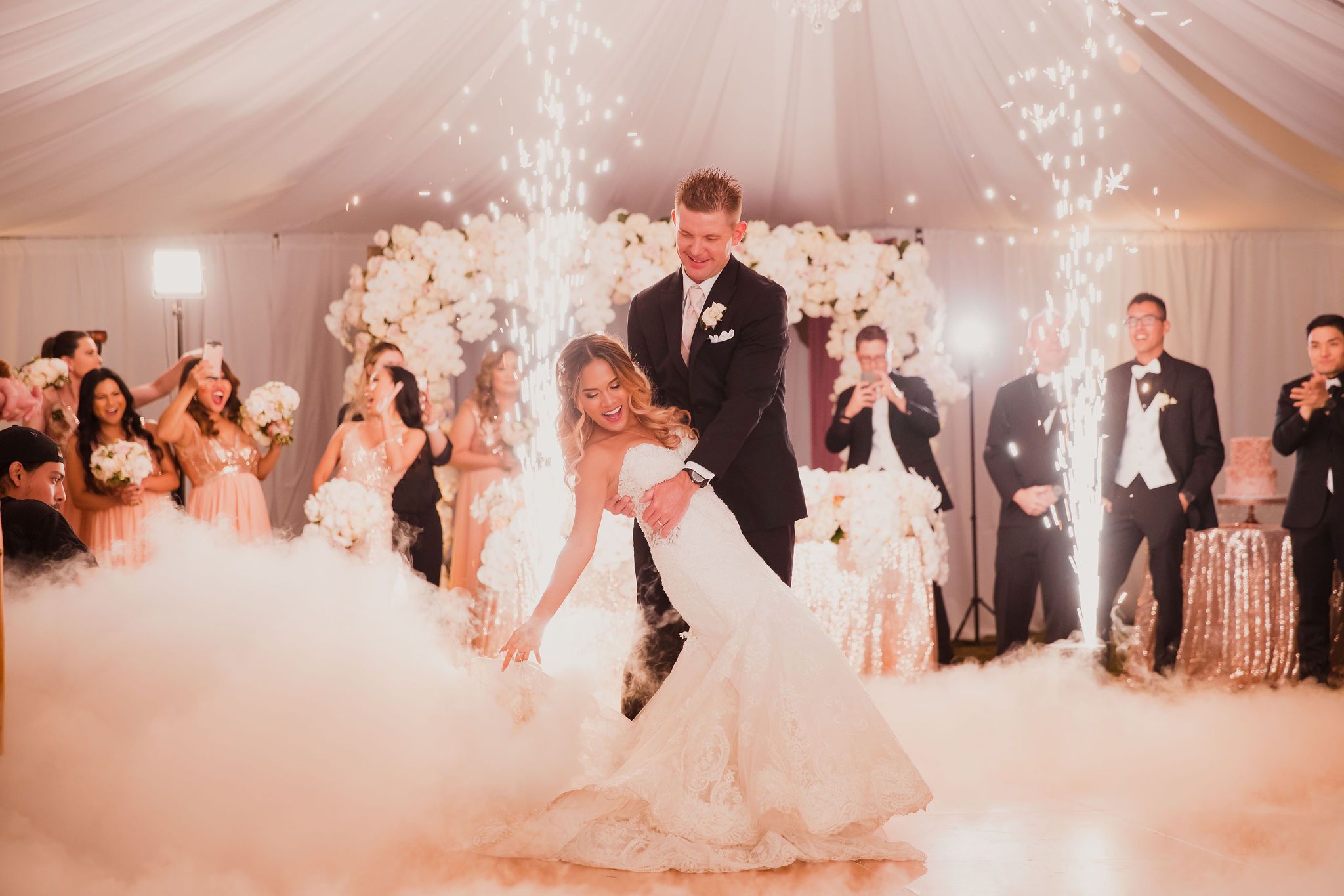 Wedding guests dance and celebrate on a pink-lit dance floor during an elegant reception celebration.