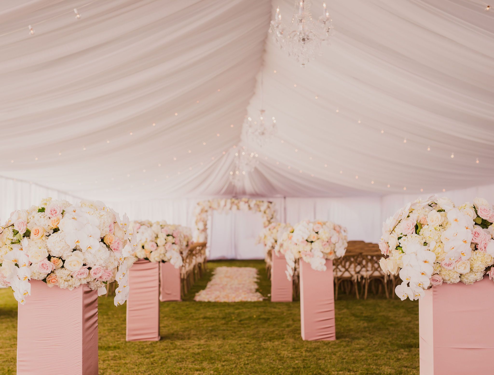 A romantic wedding tent decorated with pink accents and white floral arrangements along the ceiling.