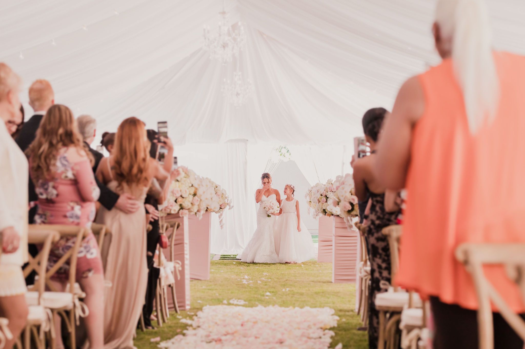 Wedding guests dance and celebrate under a large white tent during an outdoor reception.