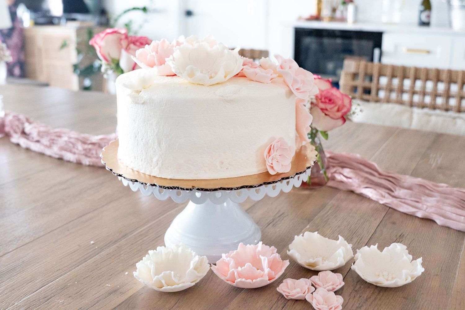 Elegant white wedding cake decorated with pink roses on a white cake stand.