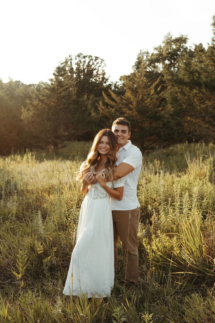 A couple embraces in a golden sunlit meadow during a romantic outdoor photoshoot at sunset.