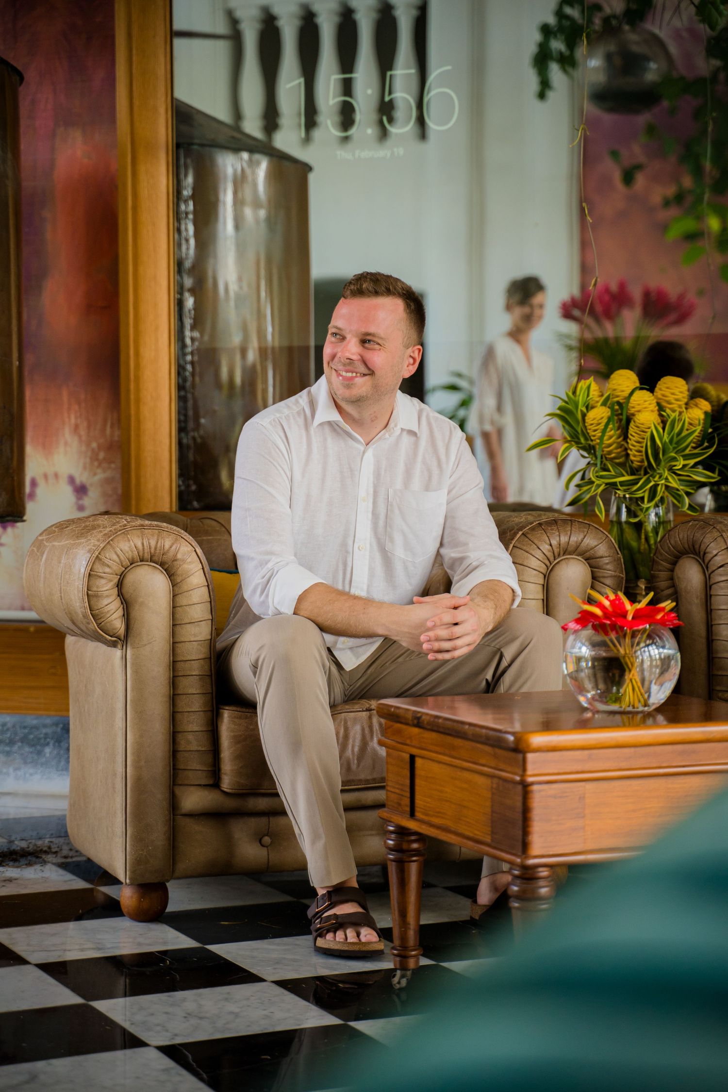 A person in white attire sits comfortably on a beige sofa next to a wooden side table with yellow flowers. Shot by Luminair Studio