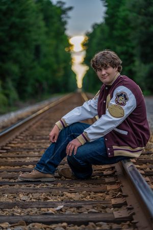 Charleston area high school senior portrait of teenage boy sitting on railroad tracks wearing letterman jacket