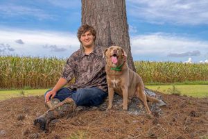High school senior portrait of teenage boy with hunting dog sitting under tree in rural South Carolina