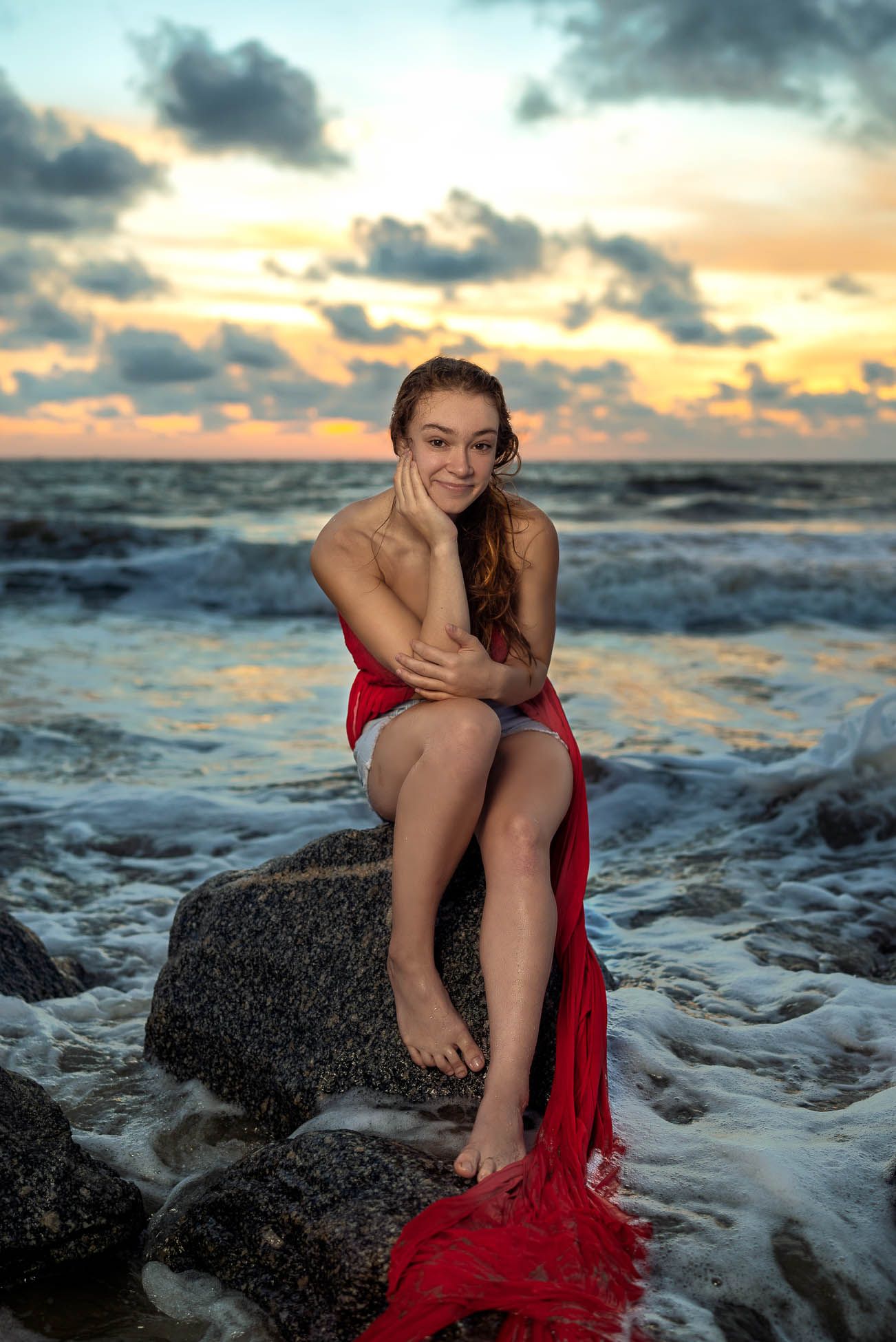 High school senior sitting on rocks at Folly Beach during sunrise for Charleston SC senior portrait photography