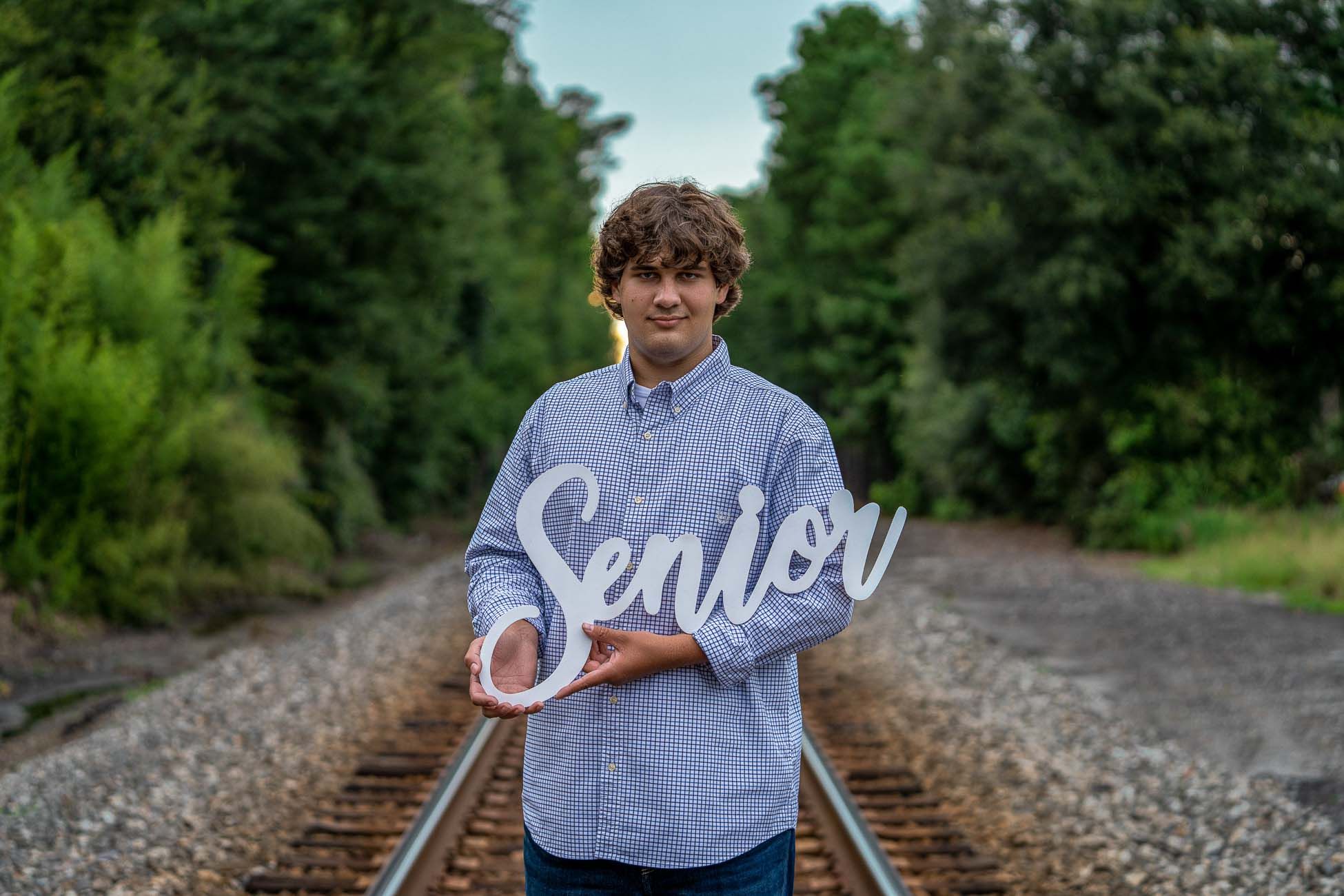 High school senior holding senior sign while posing for Charleston South Carolina senior portraits on railroad tracks