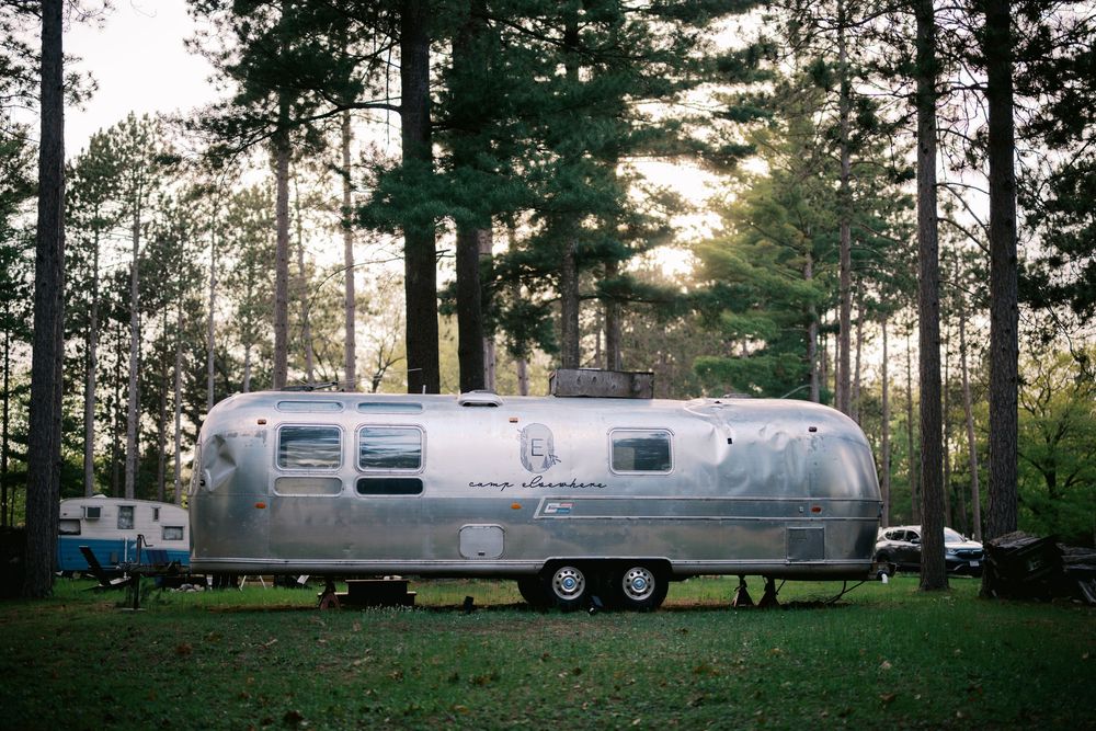 Three vintage Airstream travel trailers parked among tall pine trees at a scenic campground during sunset.