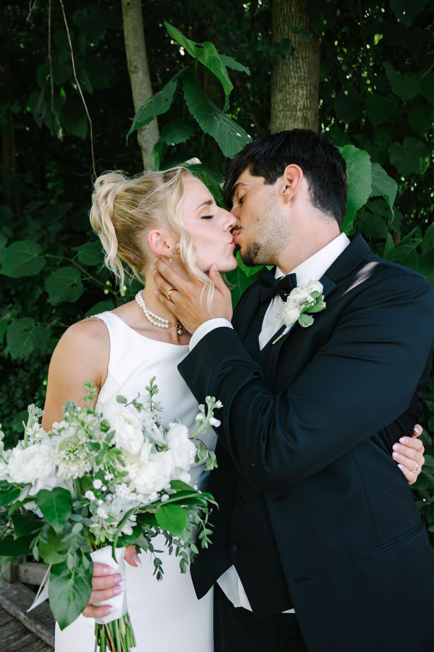 A romantic wedding moment captured with white bouquet and greenery backdrop.