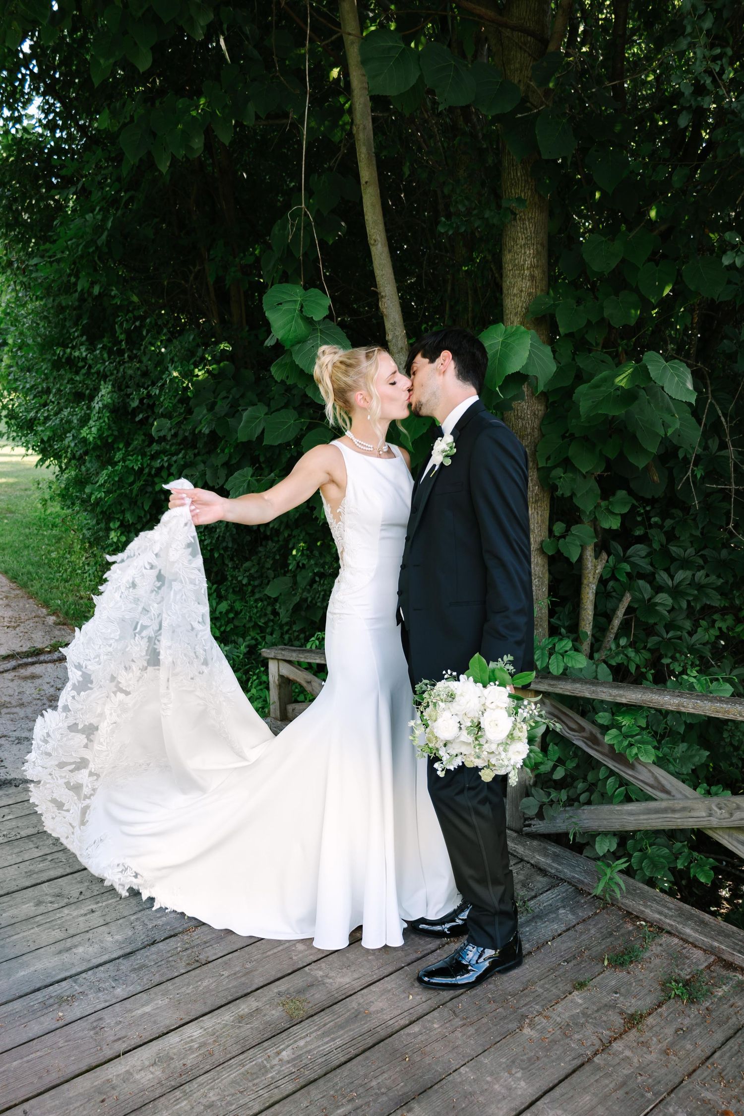 A couple shares a romantic moment on a rustic wooden deck with beautiful green trees behind them.