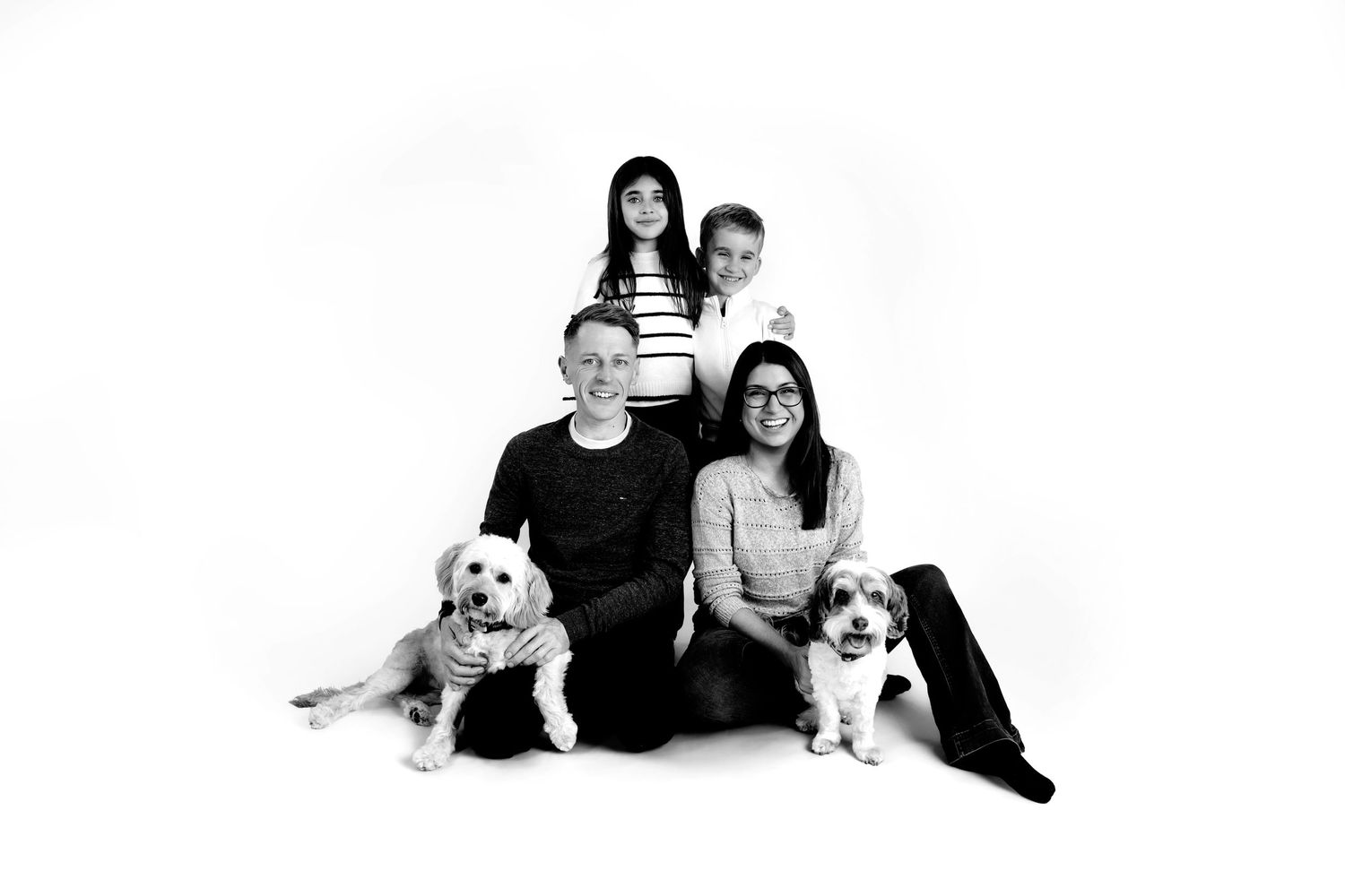 A black and white studio portrait of a group sitting together with two small white dogs.