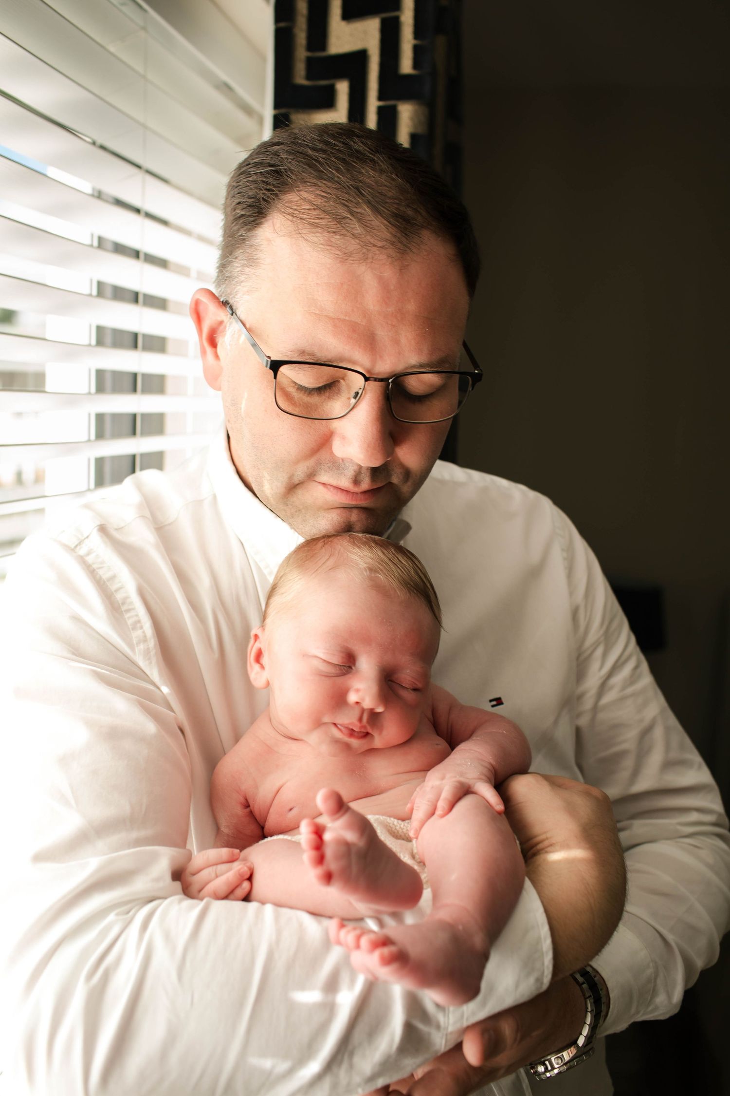 A tender moment captured in black and white as an adult cradles a sleeping newborn baby against a white background.