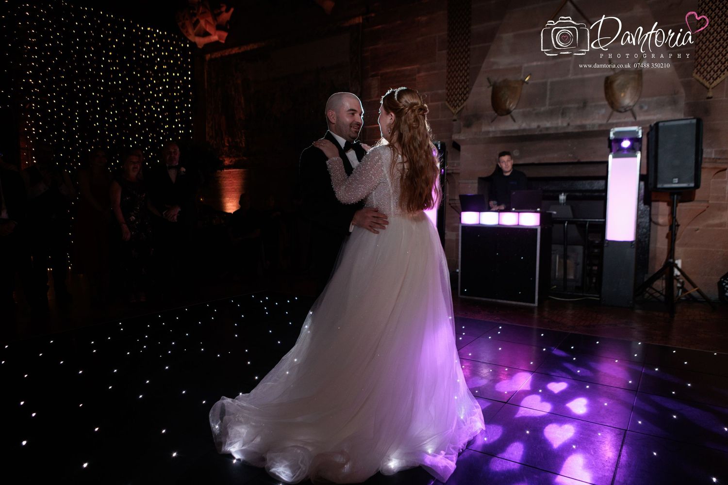 A couple shares their first dance at a wedding reception with purple lighting and sparkly decor on the dance floor.